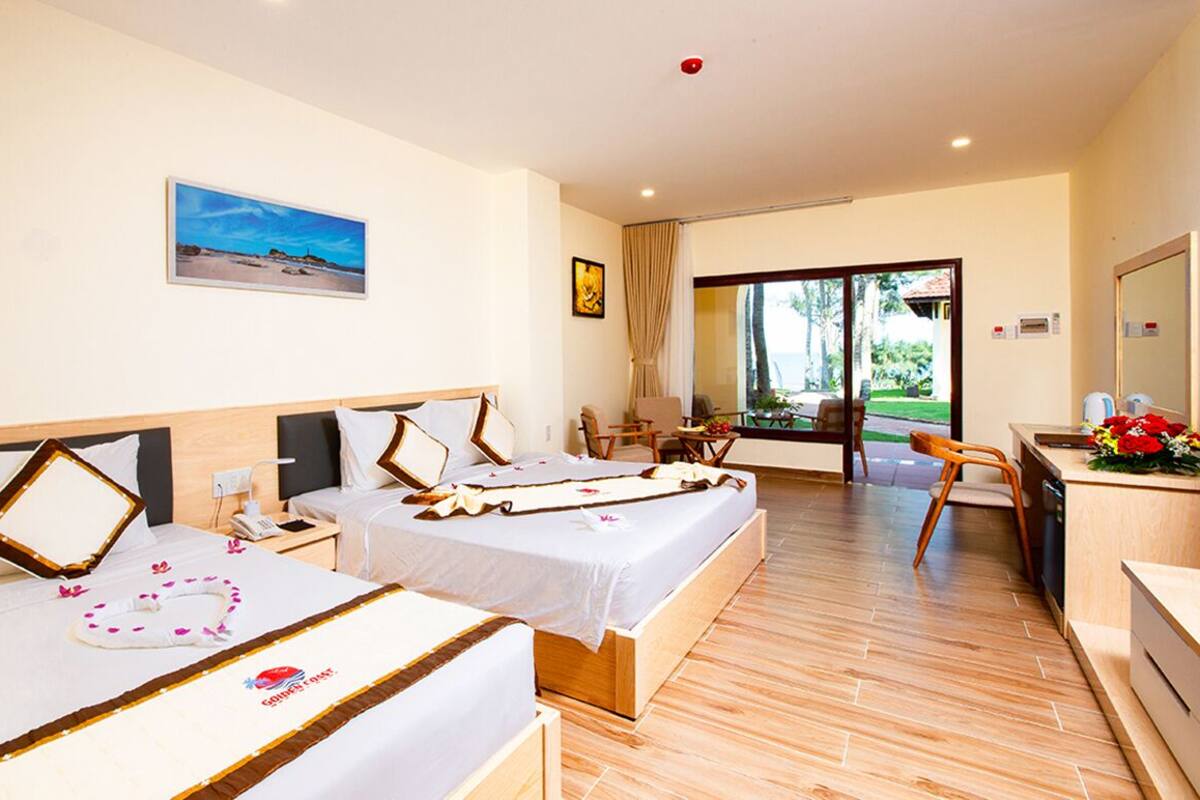 A hotel room with two beds, a desk, and a view of the outdoors.