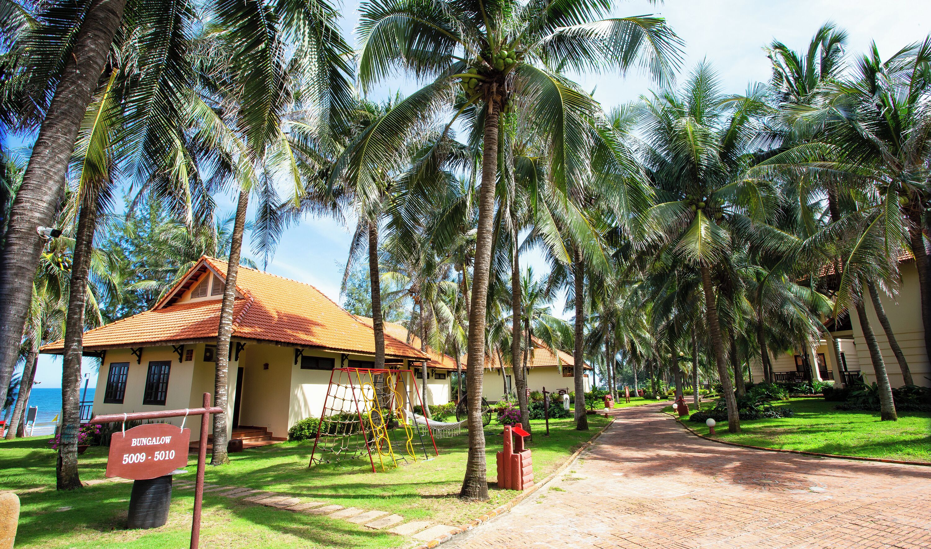 A bungalow with a tiled roof, surrounded by palm trees and a clear sky.