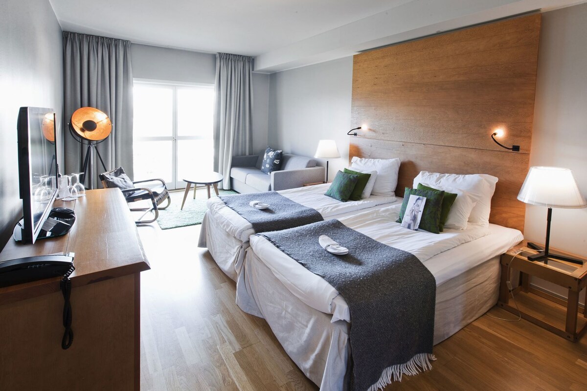 Una habitación de hotel con dos camas, un escritorio con computadora, una silla y un televisor.