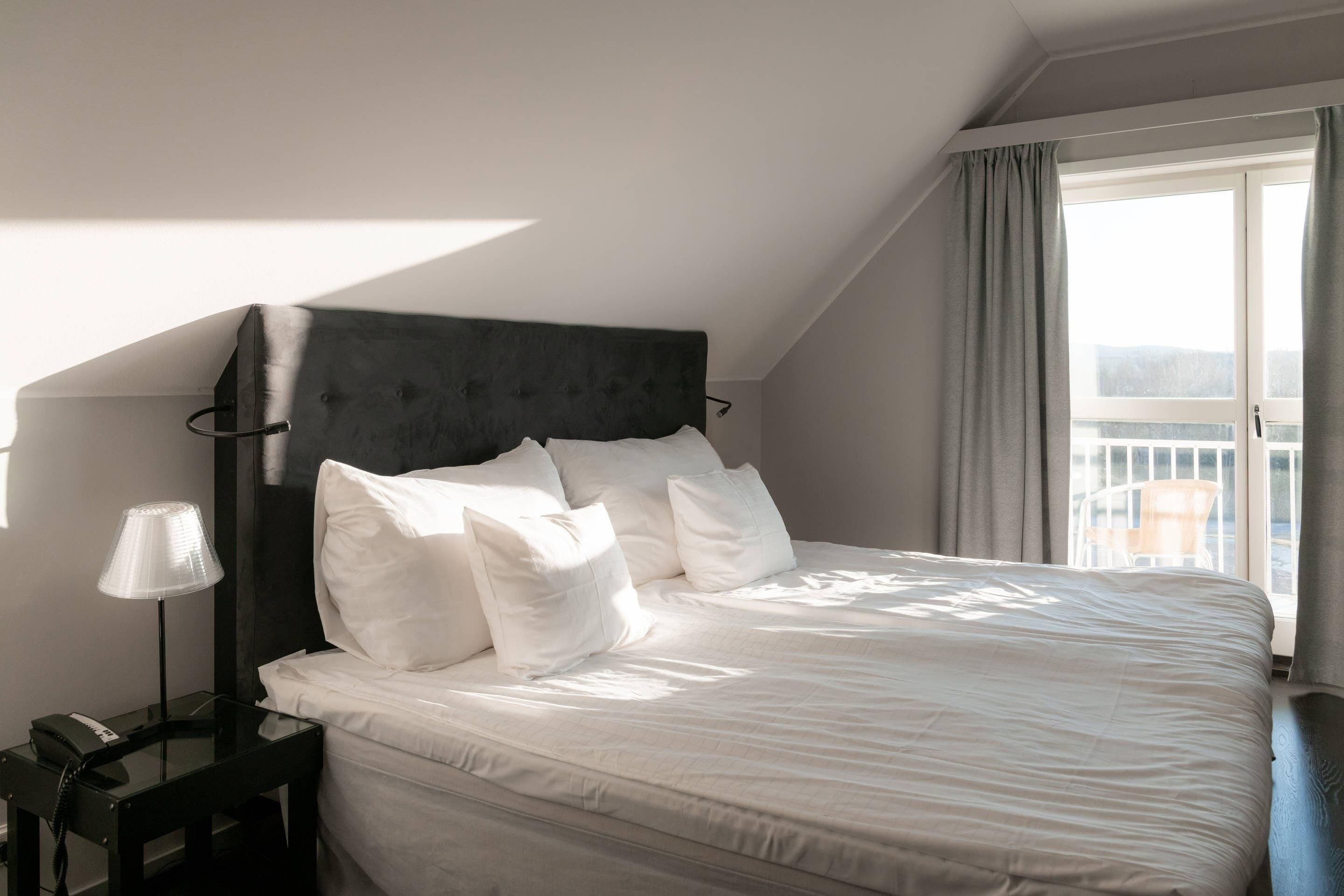 A neatly made bed with white linens and pillows, a bedside lamp, and a telephone on a small table beside the bed.