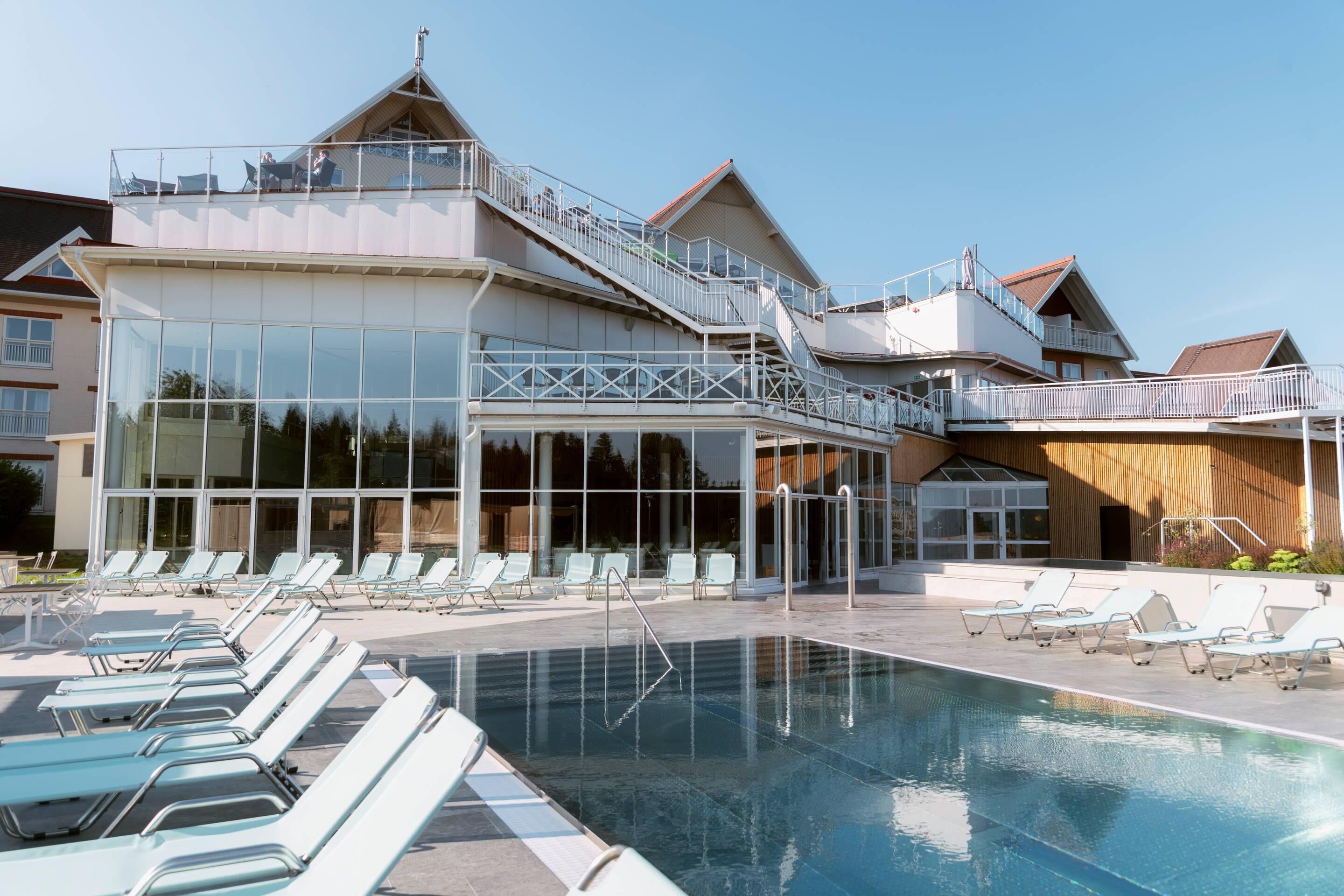 Un hôtel doté d’une piscine, de chaises longues et d’une façade en verre.