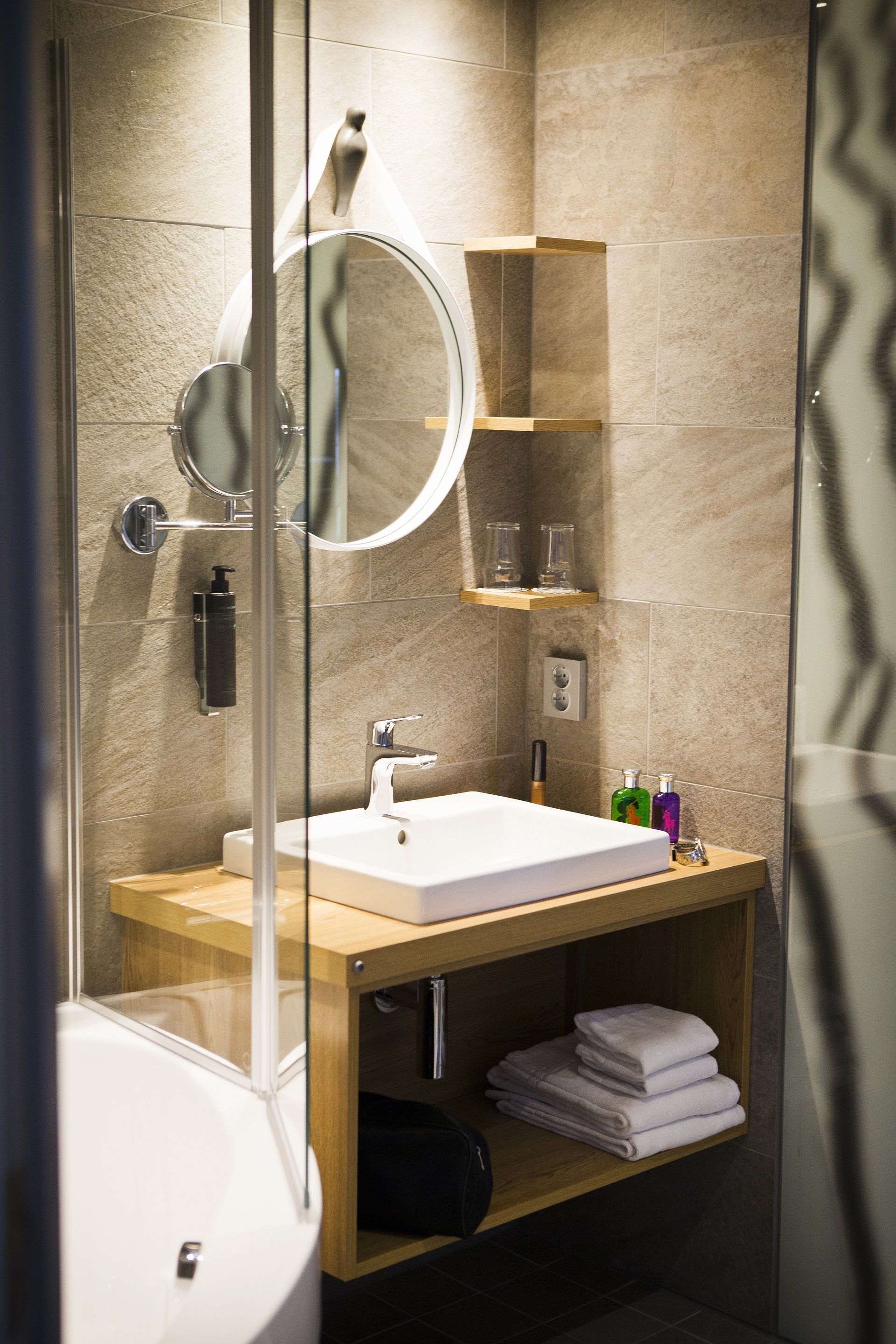 A modern bathroom with a glass-enclosed shower, a white sink, and a wooden vanity.