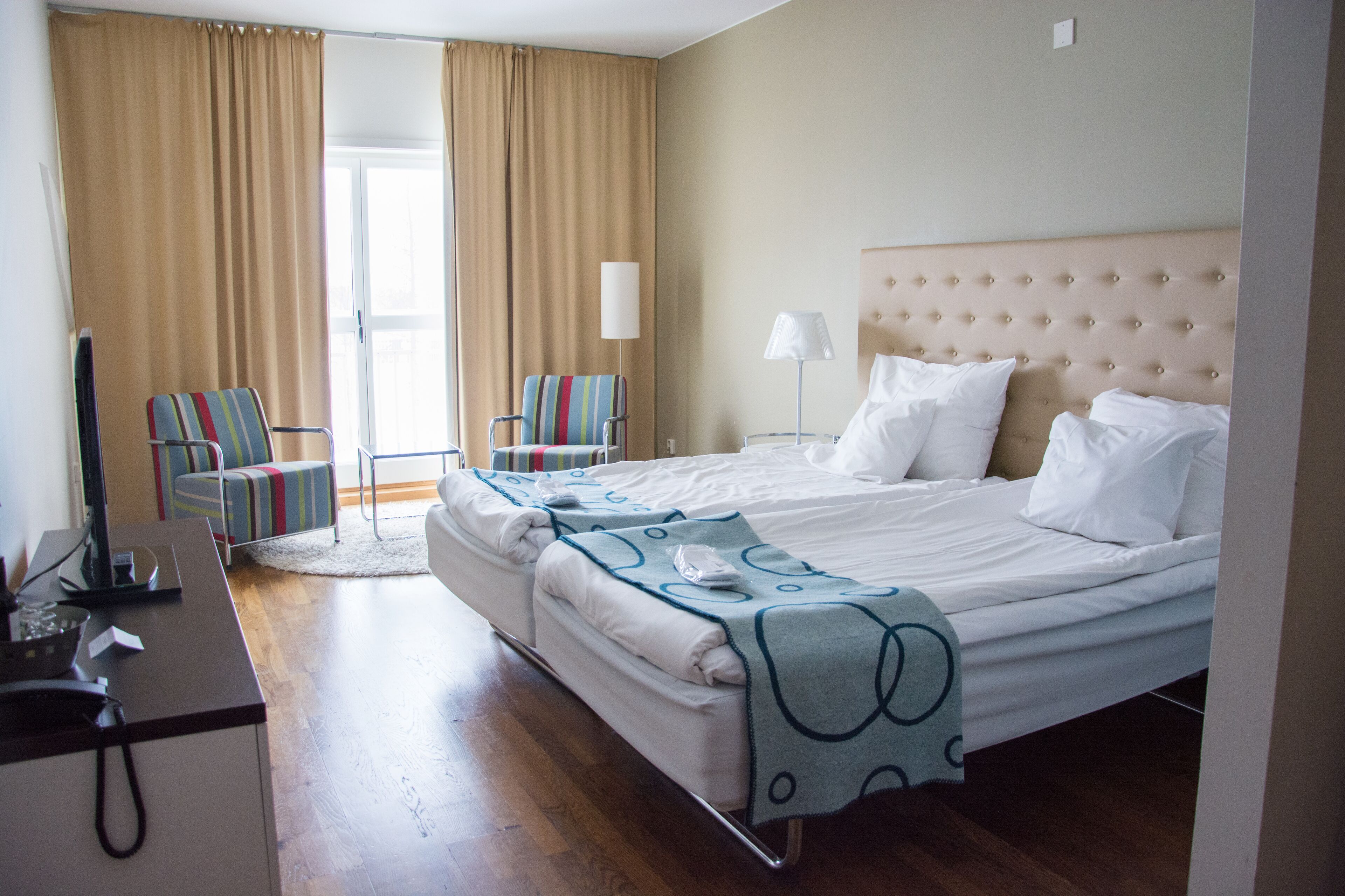 A hotel room with a bed, a desk, a chair, a lamp, and a view of the outdoors.