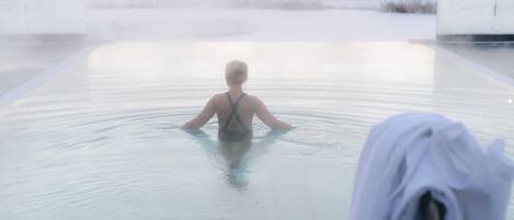 A person in a large, clear pool with a view of a snowy landscape in the background.