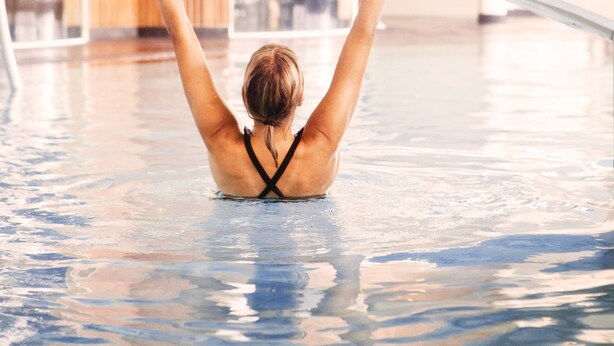 A person in a swimming pool with a wooden structure in the background. - Selma Spa+ (Sunne)