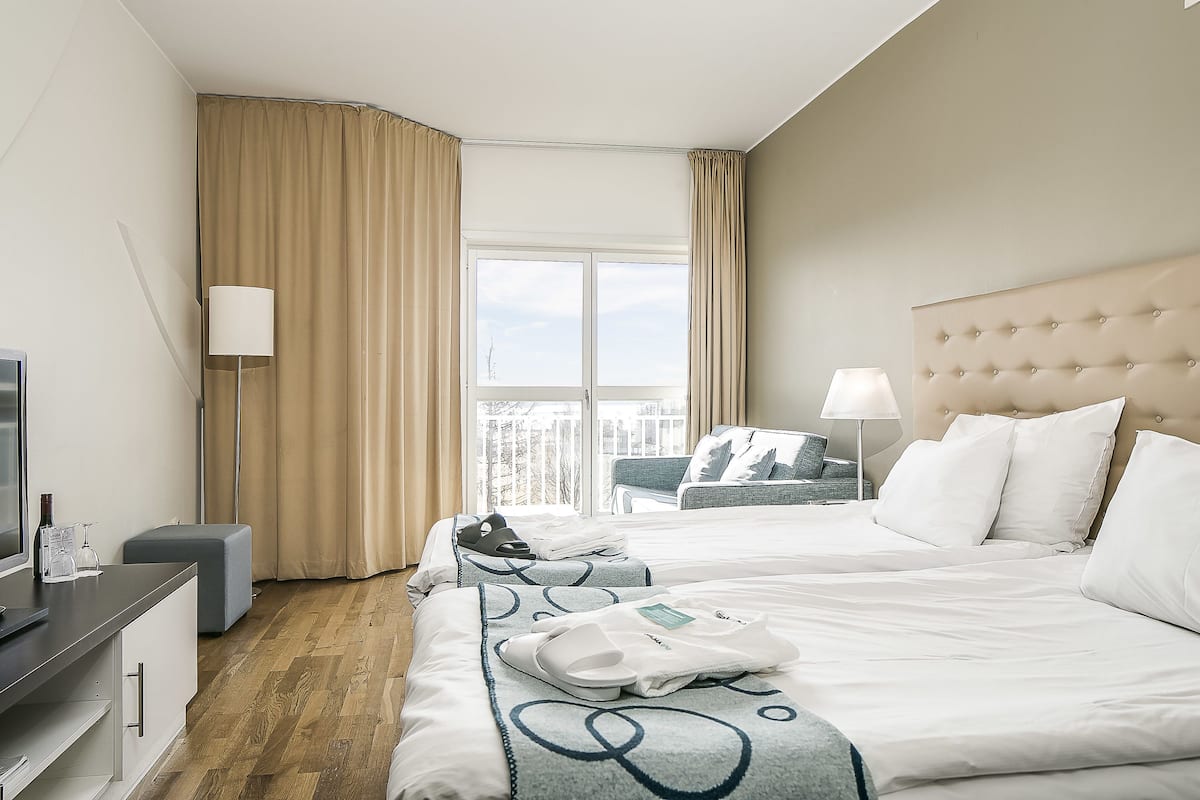 A hotel room with two beds, a desk, a chair, a lamp, and a window with curtains.