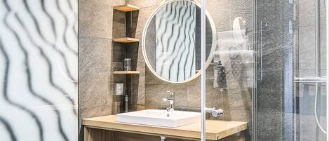 Un baño moderno con cabina de ducha de vidrio, tocador de madera y un espejo grande.