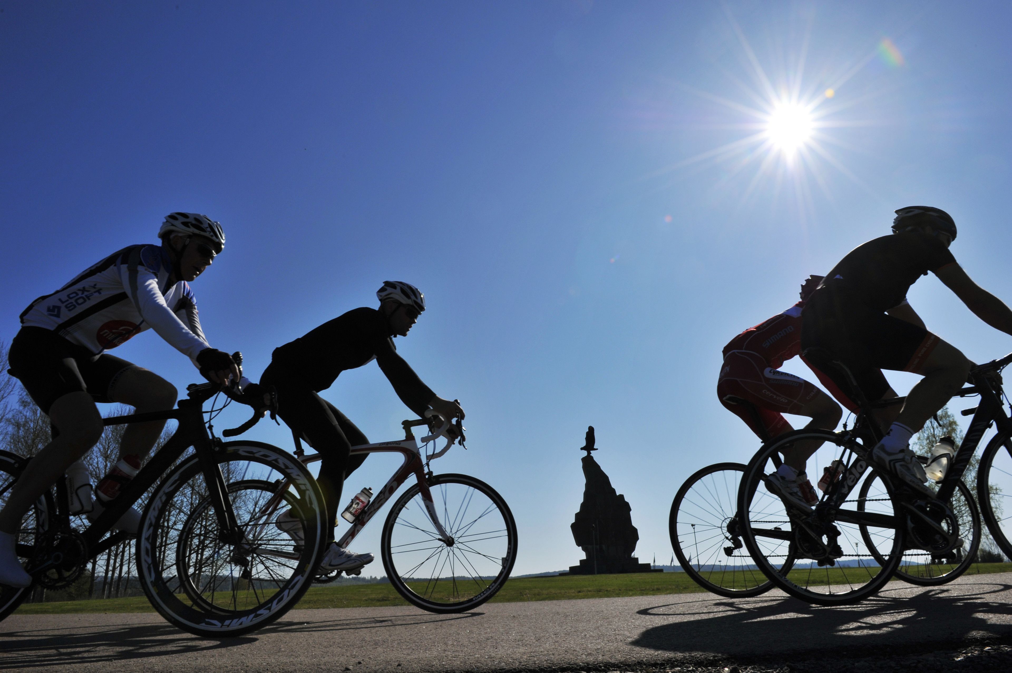 Ciclistas en una carretera con una estatua al fondo.