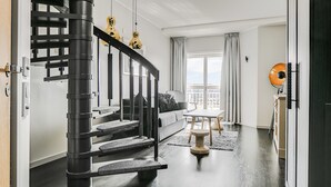 A modern living room with a black staircase, a sofa, a coffee table, and a view of the city. - Selma Spa+ (Sunne)