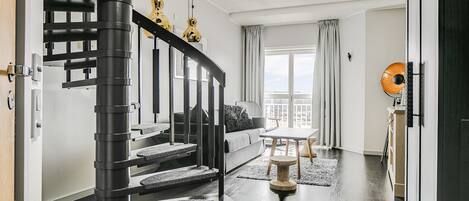 Una sala de estar moderna con una escalera negra, un sofá, una mesa de centro y vistas de la ciudad.