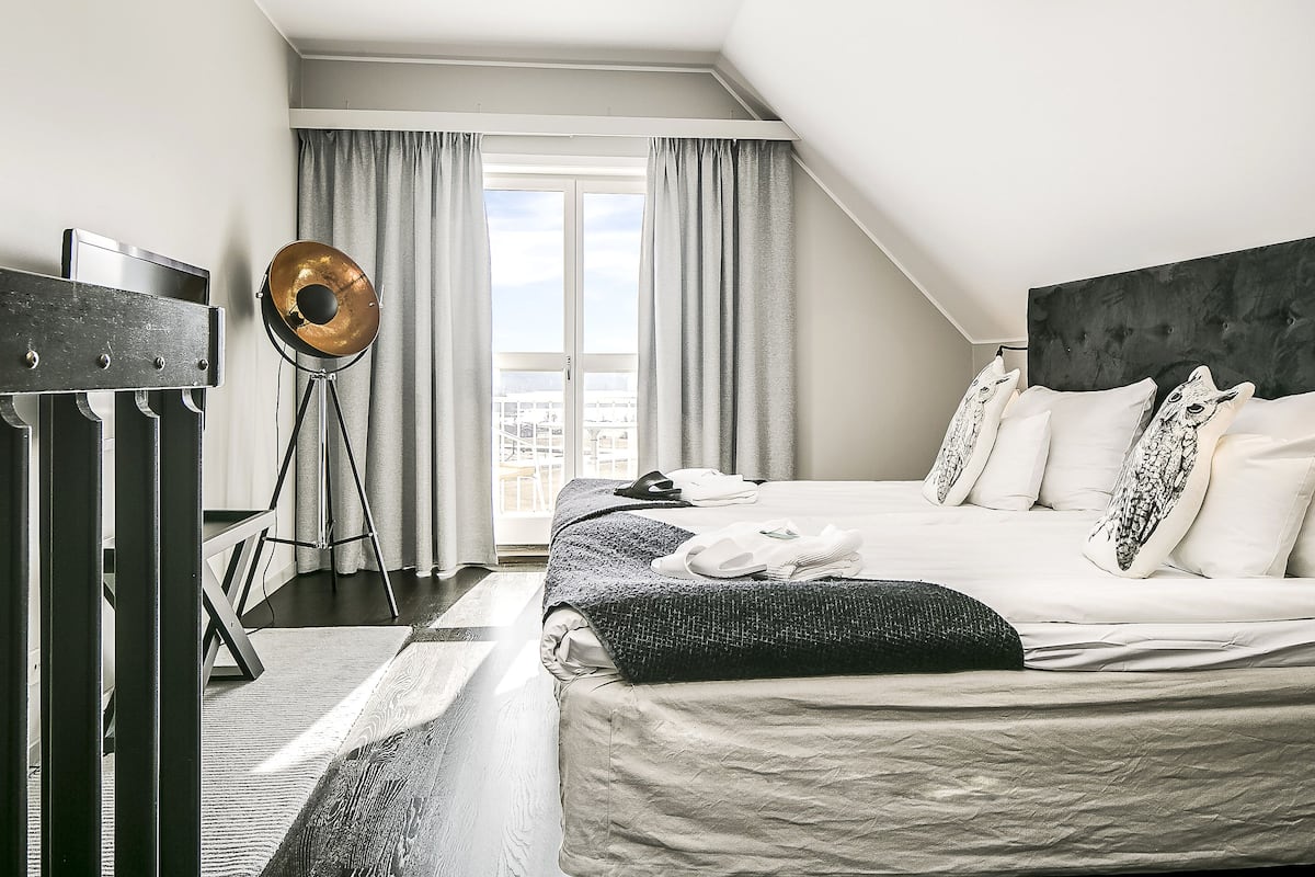 A modern hotel room with a large bed, a standing lamp, and a city view through the window.