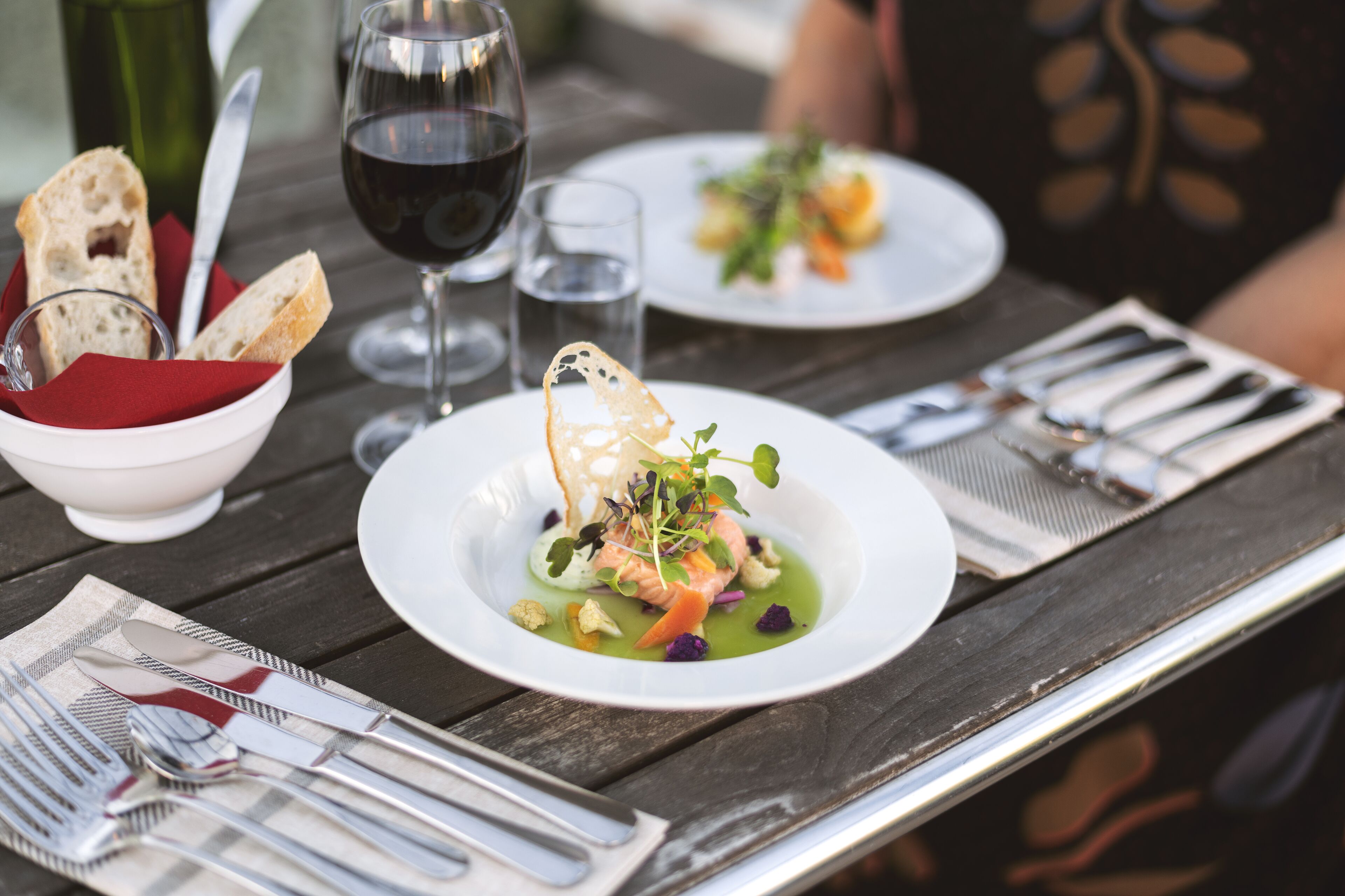 A dining table with a plate of food, a glass of red wine, and cutlery.