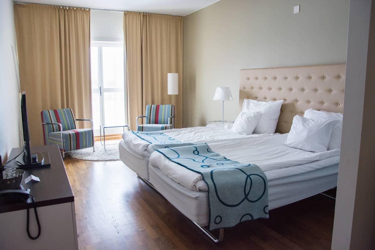 A hotel room with a bed, two chairs, a desk with a computer, and a lamp.