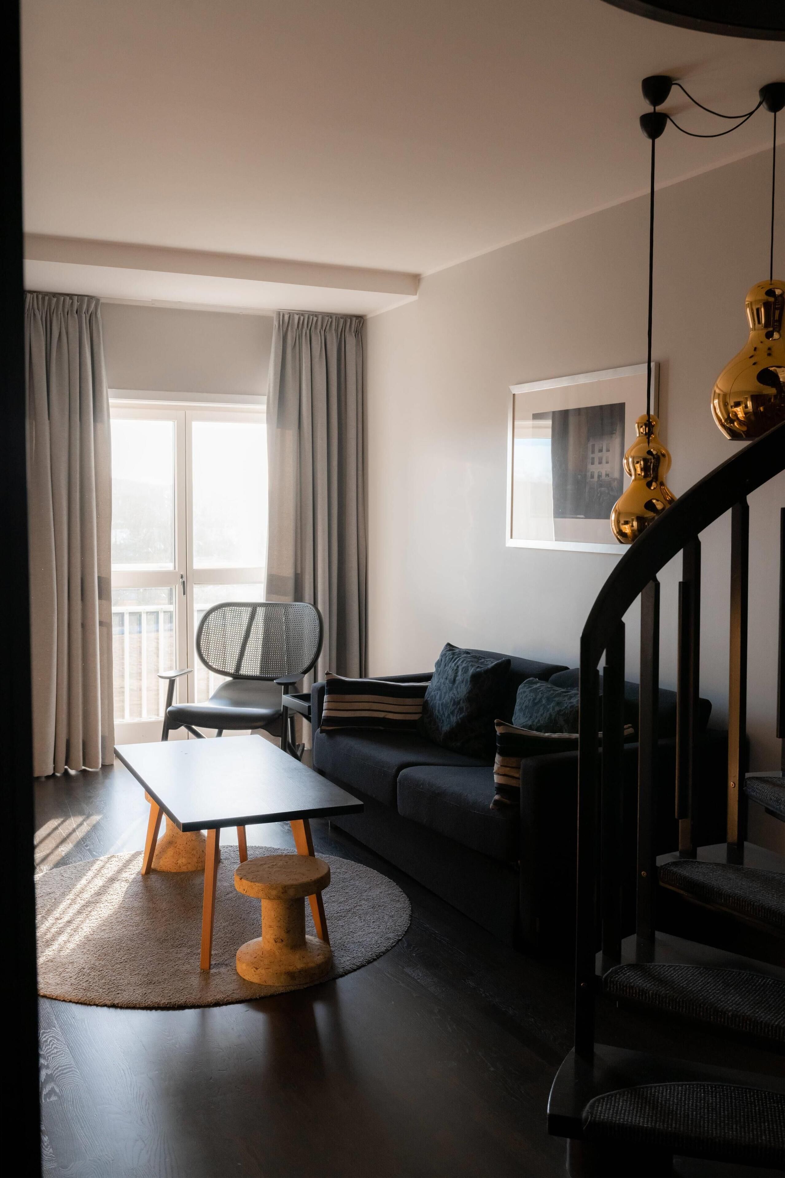 A modern living room with a sofa, a dining table, a chair, and a staircase.