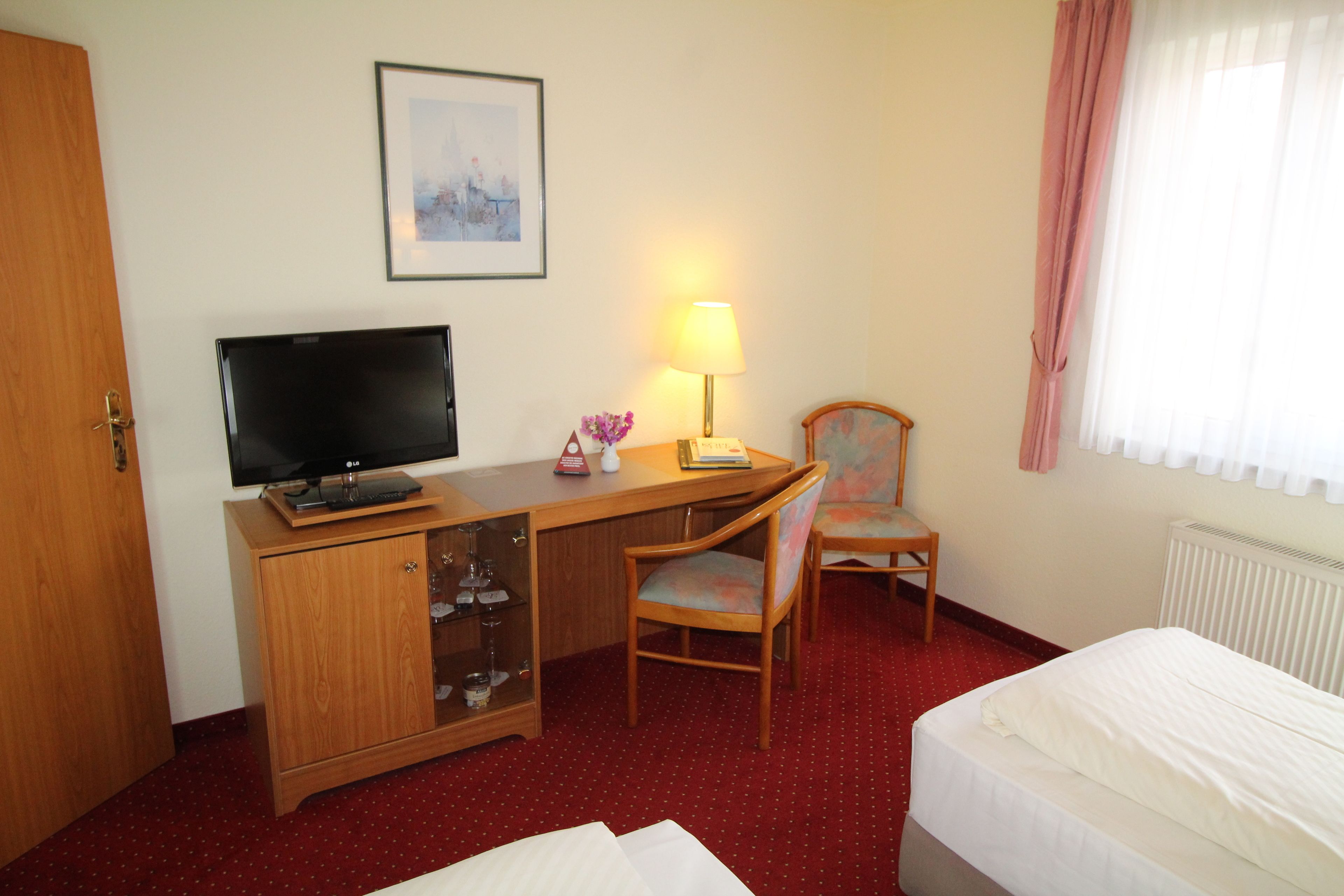 A hotel room with a wooden desk, a television, a lamp, a chair, and a bed.