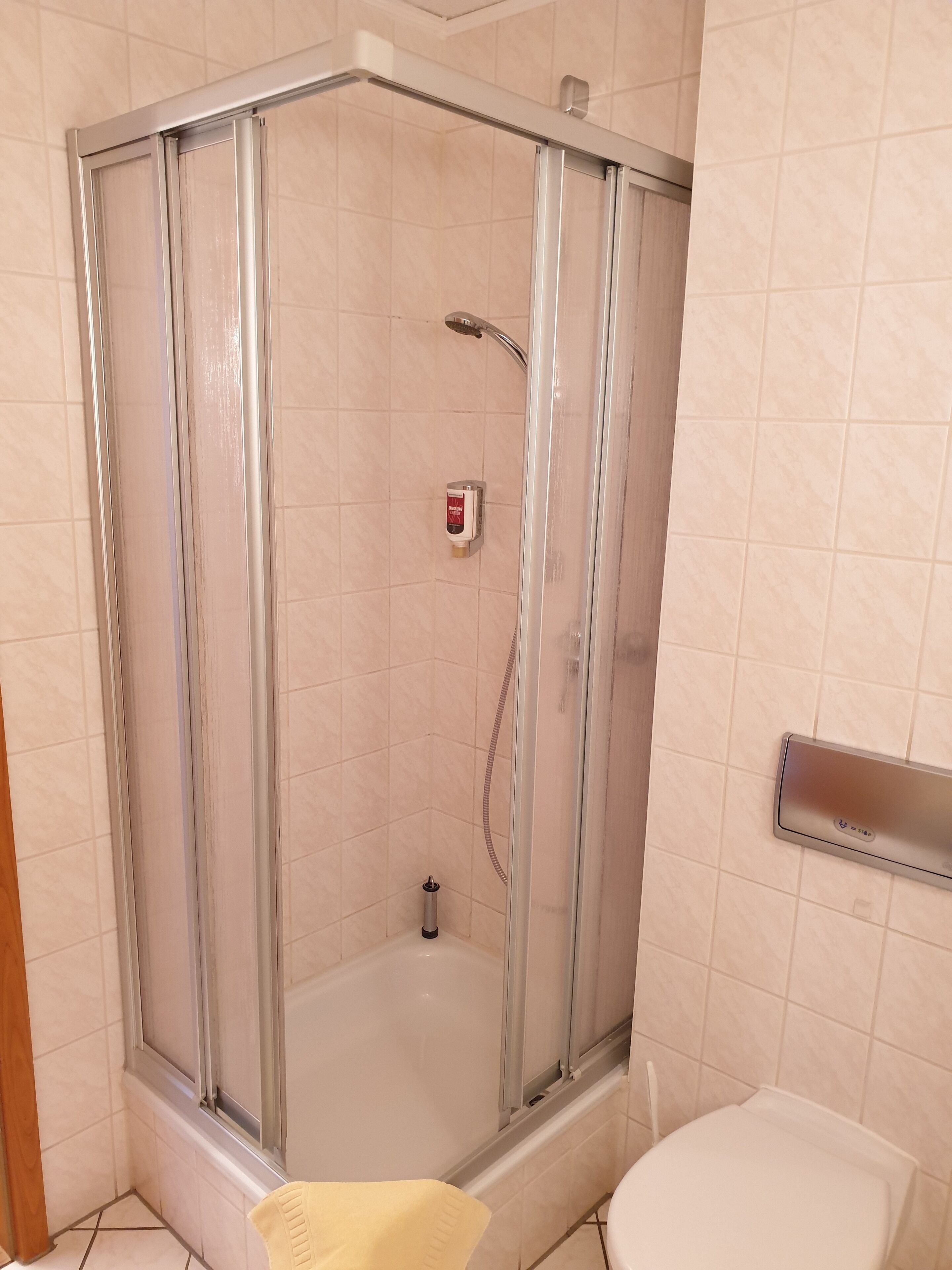 A shower area with a glass door, a handheld showerhead, and a soap dispenser.