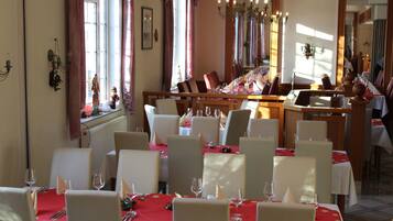 Un ristorante con diversi tavoli apparecchiati, sedie bianche e tovaglie rosse.
