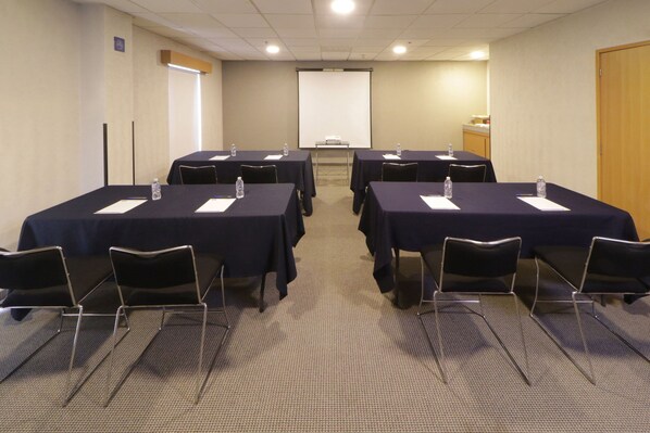 Un salón de conferencias con seis mesas, cada una con una botella de agua y papel para notas.