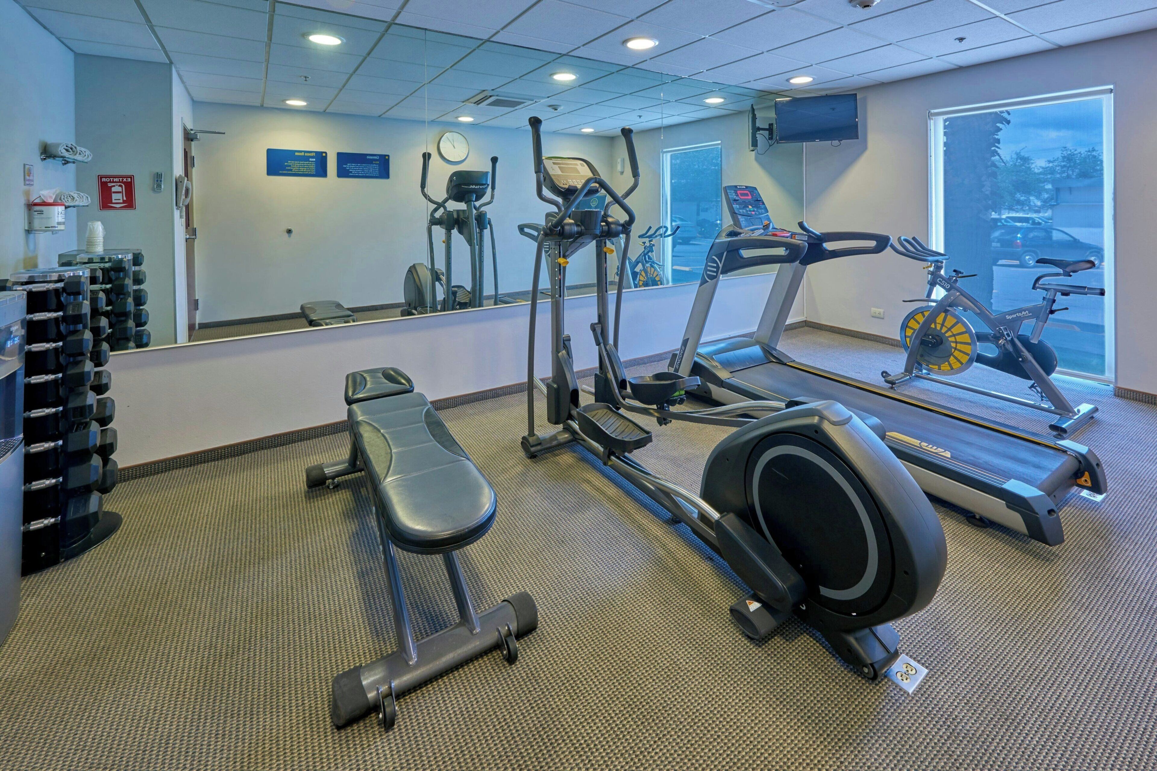 A gym with exercise equipment, a bench, and a large mirror.