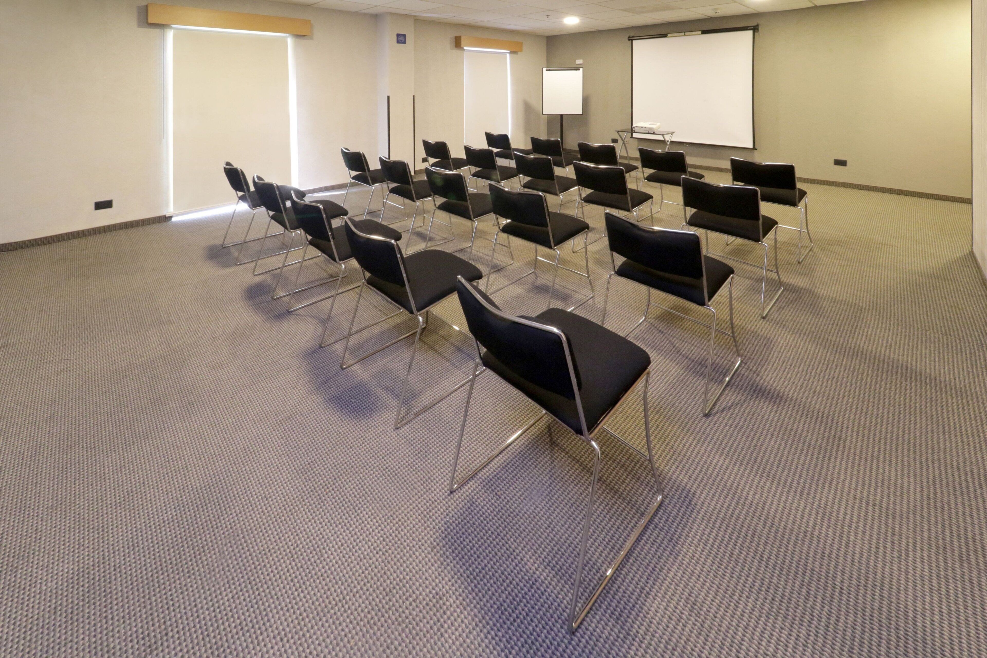 Une salle de conférence avec des rangées de chaises, un écran de projection et un tableau blanc.