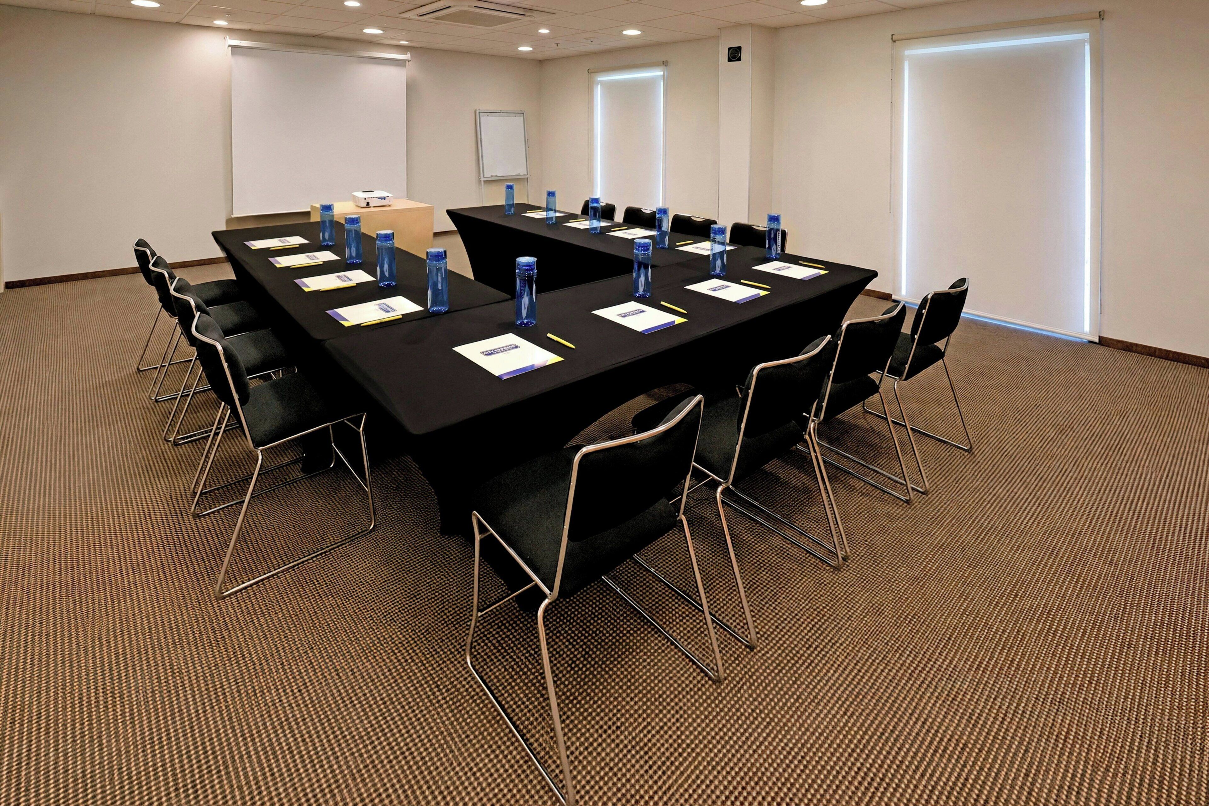 A conference room with a long table, chairs, water bottles, and a projector screen.