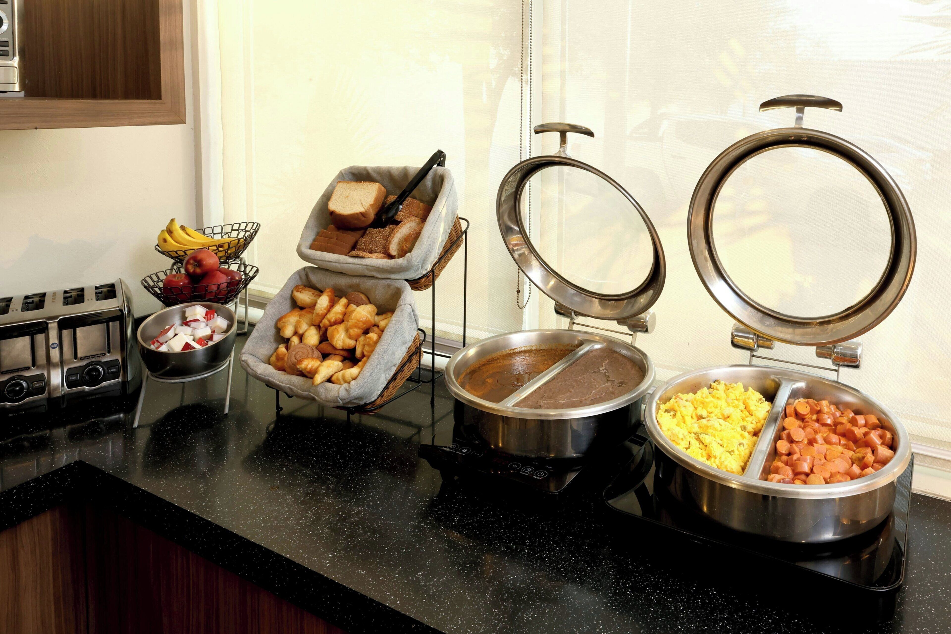 A buffet setup with various food items, including fruits, bread, and cooked dishes.