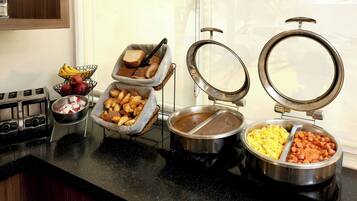 A buffet setup with various food items, including fruits, bread, and cooked dishes.