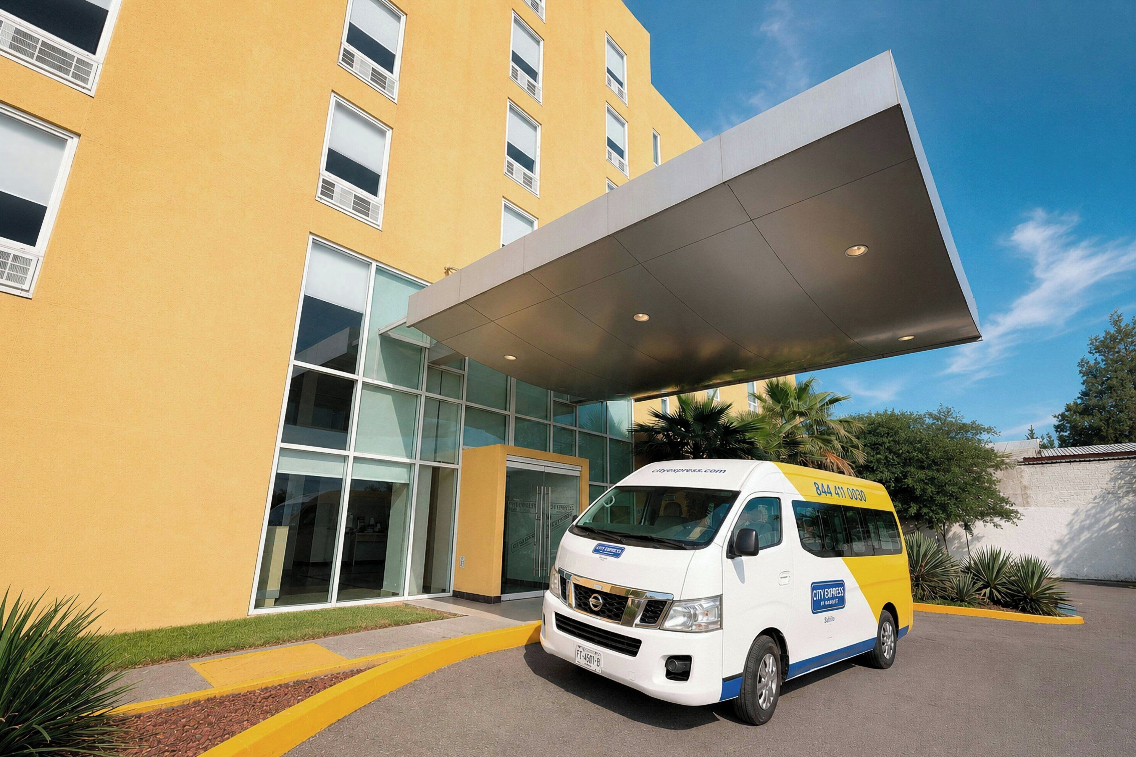 A white and yellow van parked in front of a yellow building with a glass entrance and a covered walkway.
