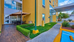 Exterior de un hotel con fachada amarilla, zona de estar al aire libre y jardín bien cuidado.
