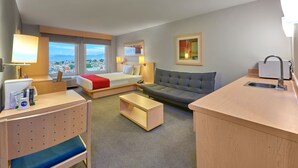 Habitación de hotel con cama, sofá, escritorio y vistas a la ciudad.