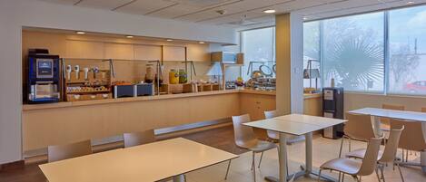 Una cafetería moderna con una barra larga, zona de mesas y amplios ventanales.