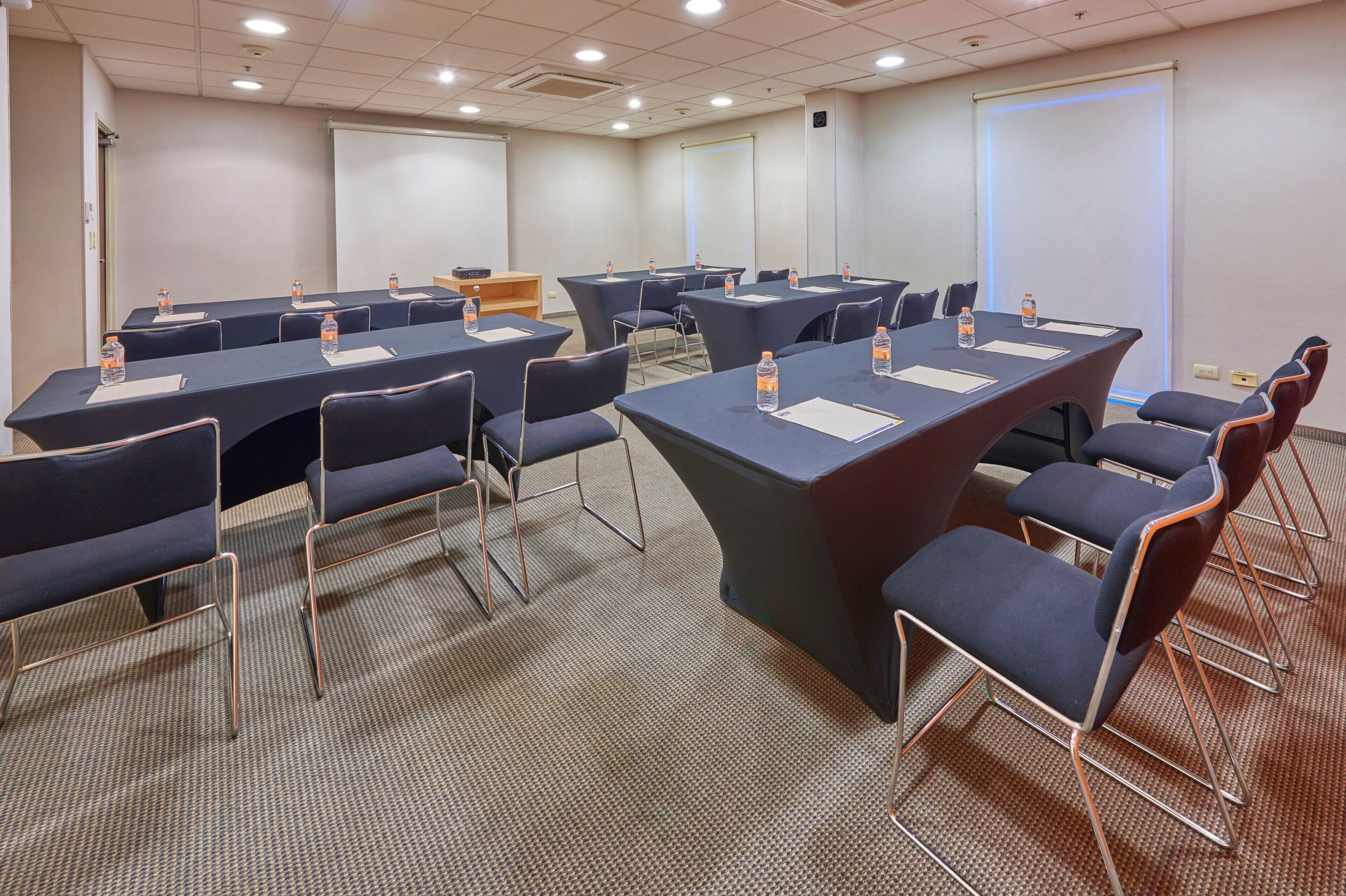 A conference room with multiple tables and chairs, equipped with water bottles and notepads.