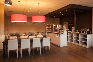 Un comedor moderno con una larga mesa y sillas, una encimera de cocina con diversos alimentos, e iluminación colgante.