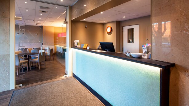 A reception area with a reception desk, a clock, and a seating area with tables and chairs. - Hotel Expo (Brussels)