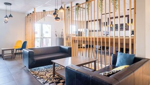 Un'area lounge moderna con divani in pelle, un pannello divisorio in legno, piante pensili e luci a sospensione.