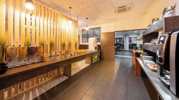 Un'area buffet con diverse postazioni gastronomiche, una macchina per caffè e una zona con sedute separate da un pannello in legno.