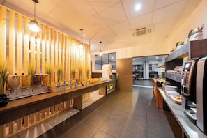 A buffet area with various food stations, a coffee machine, and a seating area with a wooden divider.