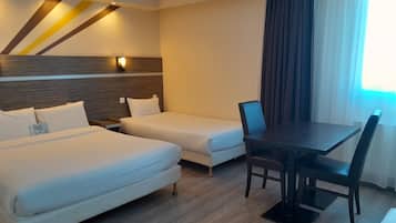Ein Hotelzimmer mit zwei Betten, einem Esstisch mit Stühlen und einem großen Fenster mit Vorhängen.