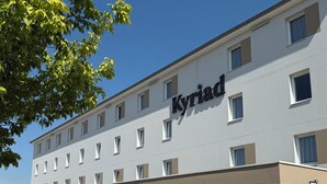 Un hotel con un cartello che riporta la scritta "Kyriad" sulla facciata. Davanti all'edificio ci sono tavoli e sedie all'aperto.