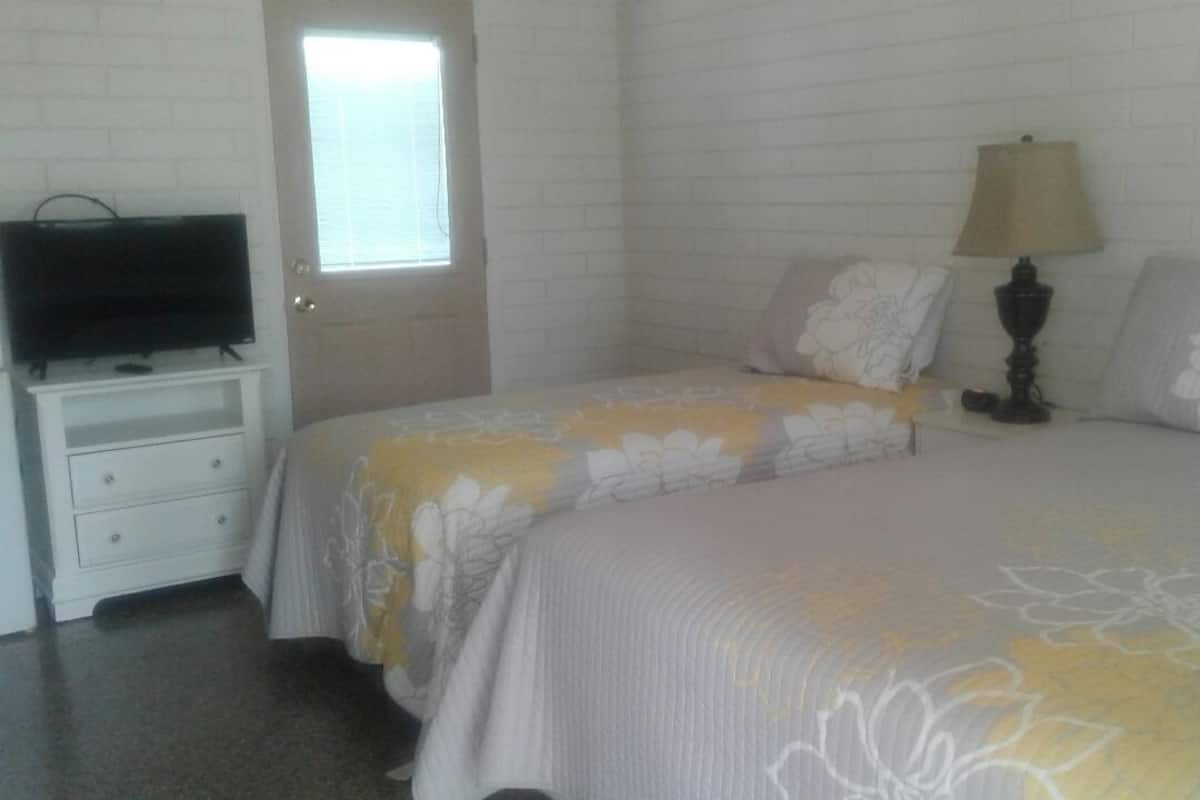 A bedroom with two beds, a television on a nightstand, and a lamp on a table.