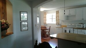 A kitchen with white cabinets, a wooden countertop, and a dining area with chairs and a table. - Astor Bridge Marina & Motel (Astor)