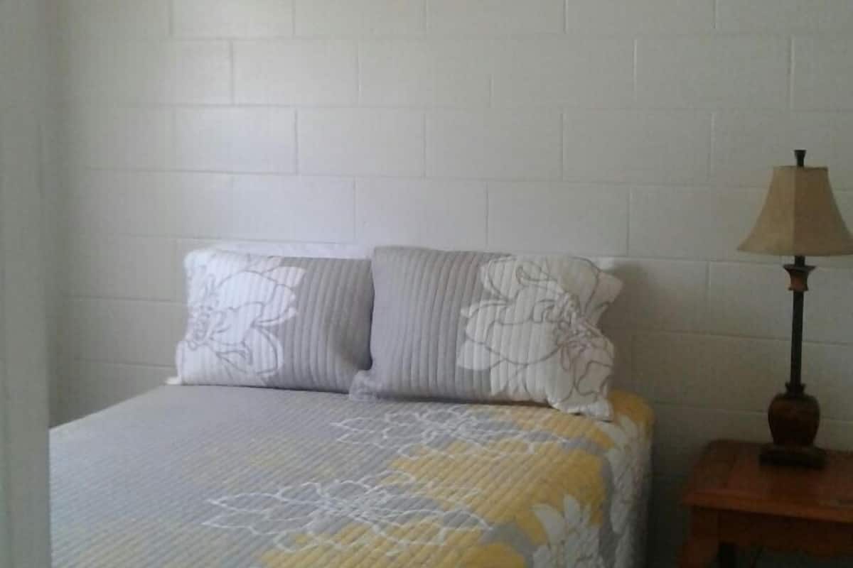A bedroom with a bed, two pillows, a lamp, and a white brick wall.
