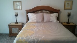 A bed with a floral bedspread, two bedside tables with lamps, and framed pictures on the walls. - Astor Bridge Marina & Motel (Astor)