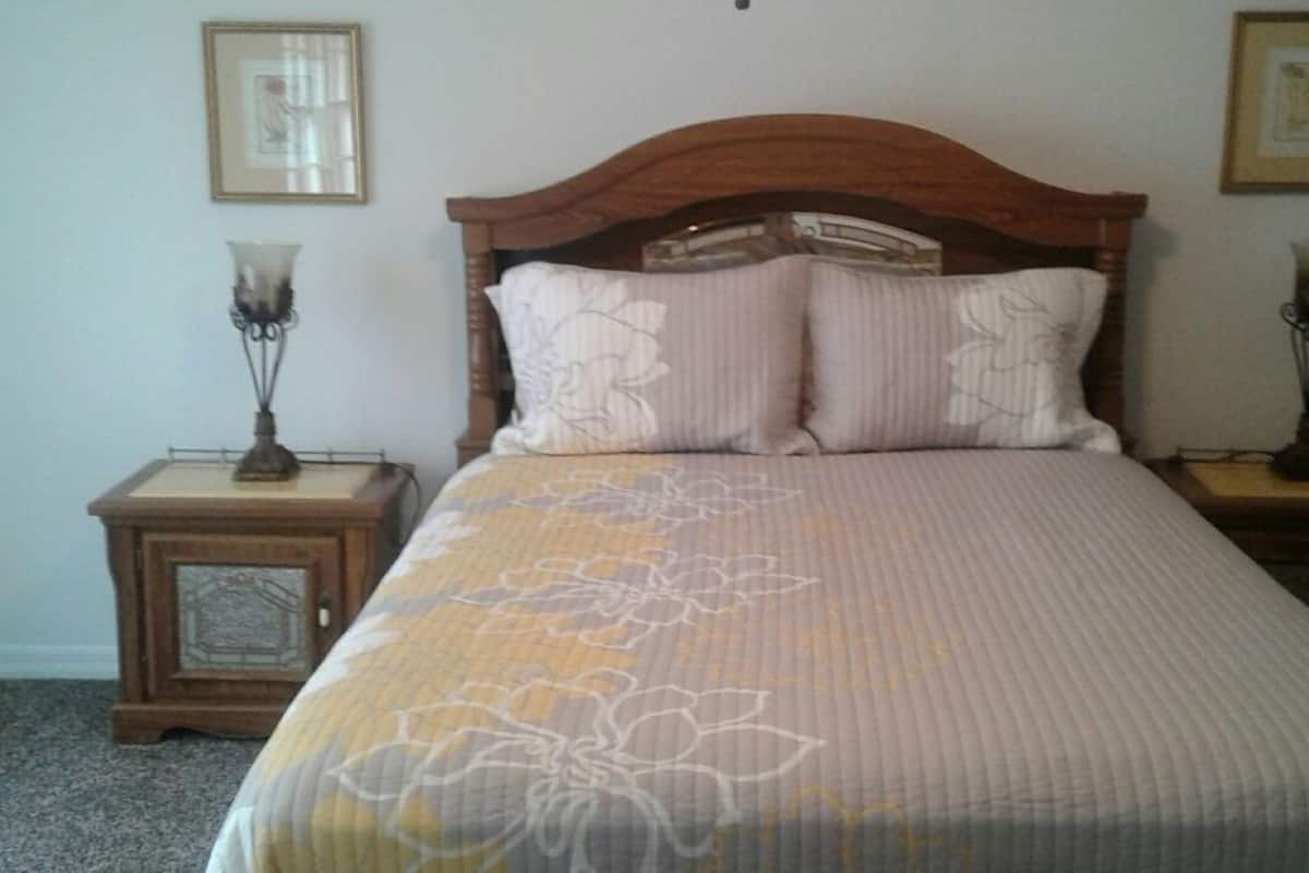 A bed with a floral bedspread, two bedside tables with lamps, and framed pictures on the walls.
