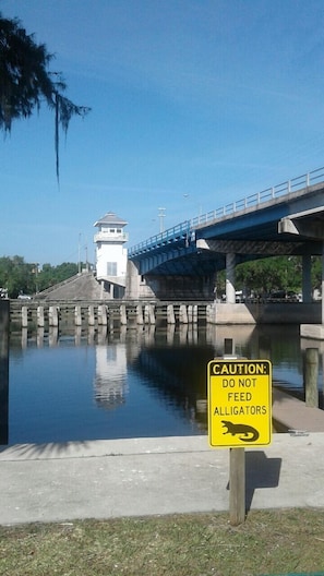 A bridge over a calm body of water with a caution sign warning against feeding alligators. - Astor Bridge Marina & Motel (Astor)