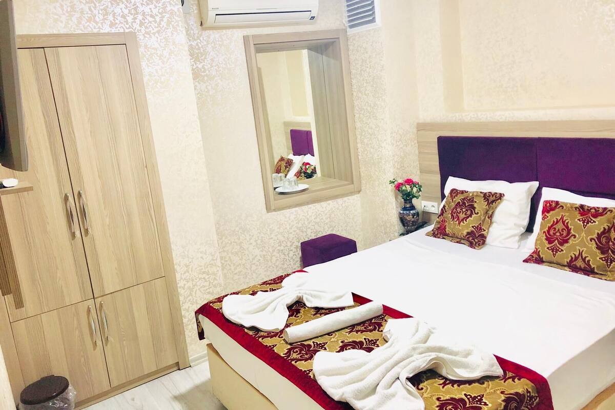Hotellihuone, jossa on sänky, vaatekaappi, peili ja ilmastointilaite.