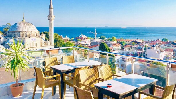 Terraço com mobiliário de vime e vista para a paisagem urbana, incluindo uma mesquita e um minarete.