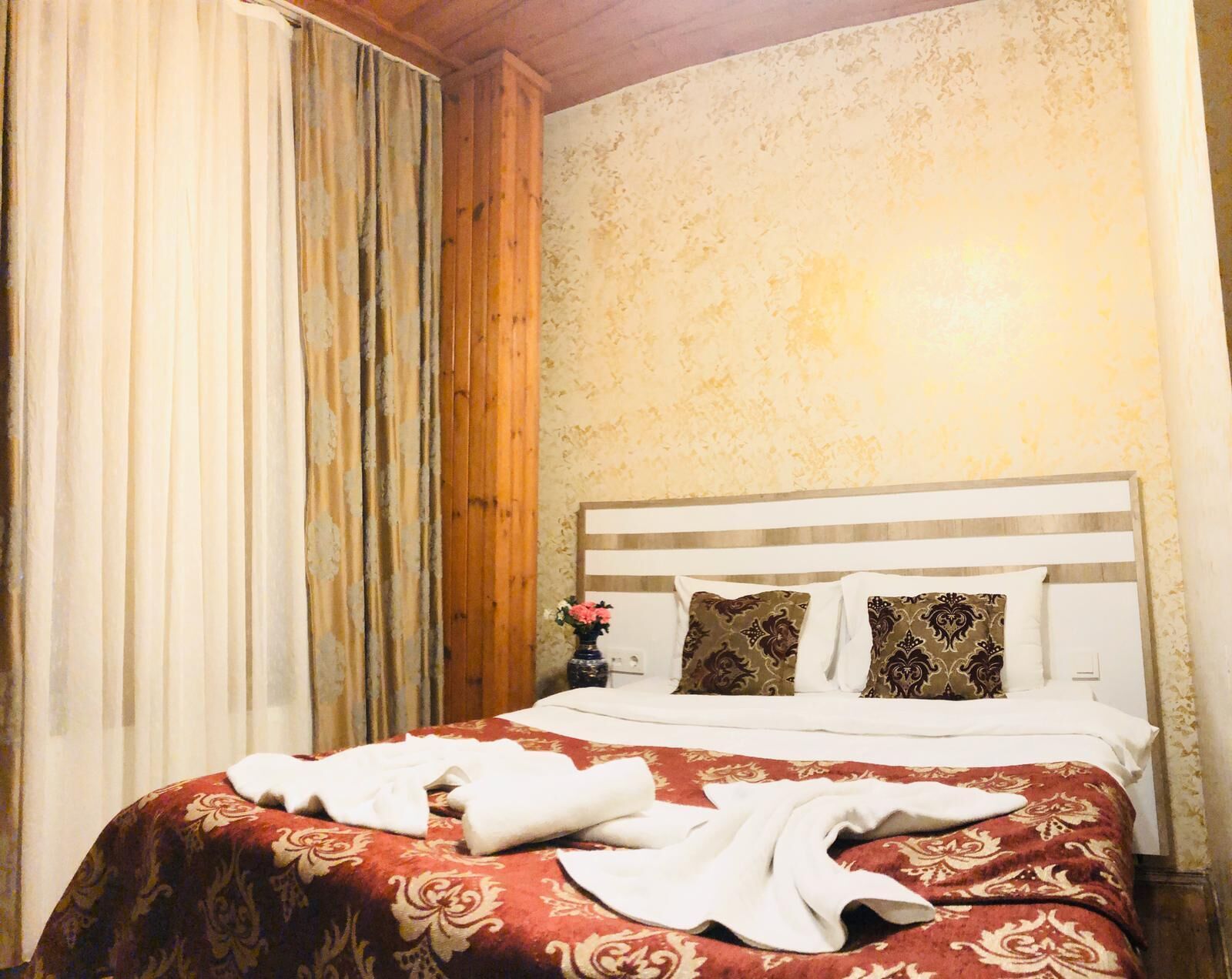 A hotel room with a bed, a nightstand, and a vase with flowers.