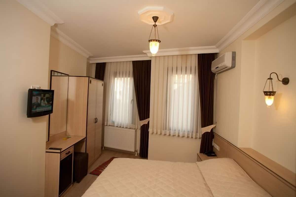 Hotellihuone, jossa on sänky, työpöytä, peili, televisio ja ikkuna, jossa on verhot.
