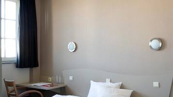 A hotel room with a bed, a desk, a chair, and a window with curtains.